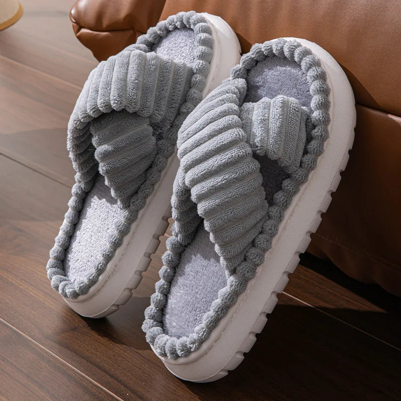 Pair of gray slippers with white soles on a wooden floor.